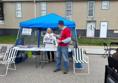 A booth at JazzFest 2023 displaying promotional materials, with two people engaging in conversation and folding chairs nearby.